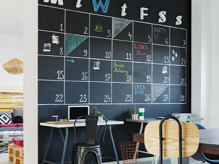 Office with a black chalkboard wall used as a calendar.